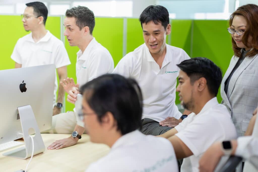 A group of people in white shirts collaborating around a computer, discussing software development processes and methods.